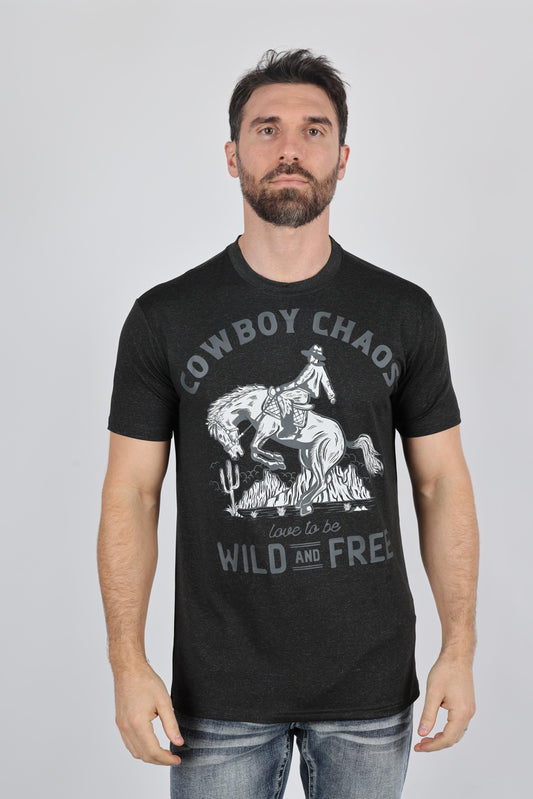 A man wearing a black graphic t-shirt with a white western print of a cowboy on a bucking horse and the text 'COWBOY CHAOS love to be WILD AND FREE', paired with blue jeans, against a solid gray background.