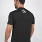 A man wearing a dark charcoal gray t-shirt with a small white graphic on the upper back, shown from a rear three-quarter view against a light gray studio background.