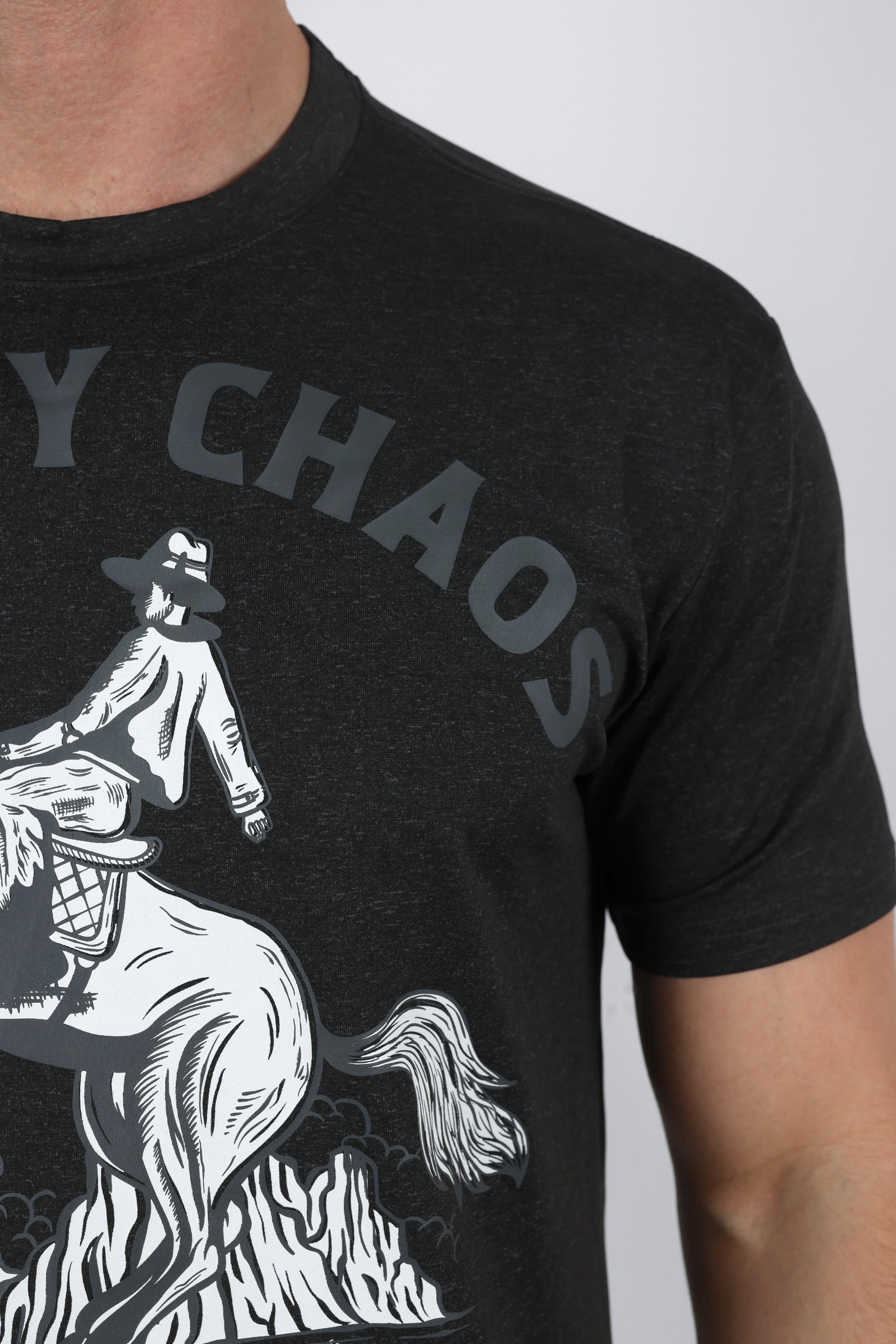 Close-up of a person wearing a dark charcoal heather t-shirt with a graphic print of a cowboy riding a bucking horse and the text 'MY CHAOS' in gray.
