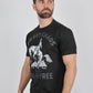 A man wearing a black graphic t-shirt with a white cowboy print and text reading 'COWBOY CHAOS' and 'ALL FOR FREE', paired with blue jeans, against a plain light gray background.
