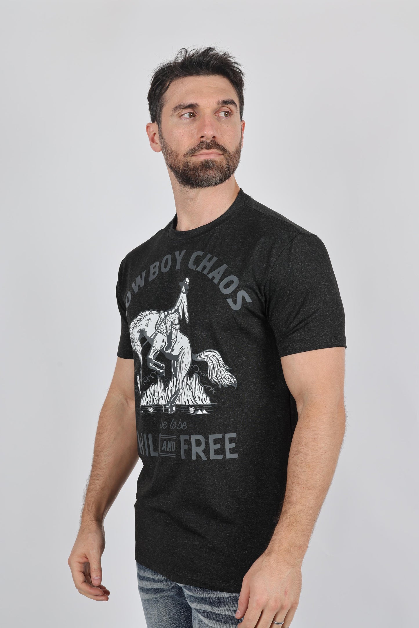 A man wearing a black graphic t-shirt with a white cowboy print and text reading 'COWBOY CHAOS' and 'ALL FOR FREE', paired with blue jeans, against a plain light gray background.