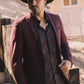 Man wearing a burgundy blazer and cowboy hat in a rustic setting