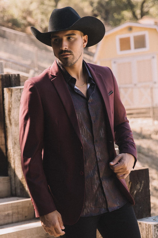Man wearing a burgundy blazer and cowboy hat in a rustic setting