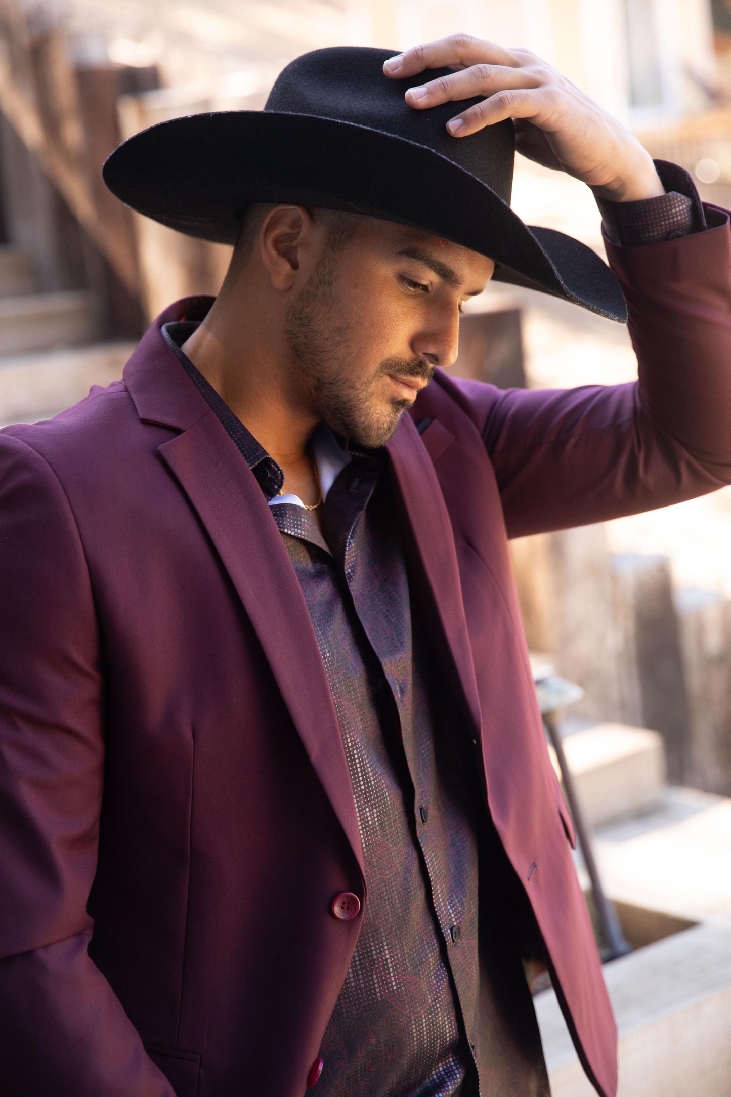 Man wearing a dark cowboy hat and burgundy blazer in an outdoor setting