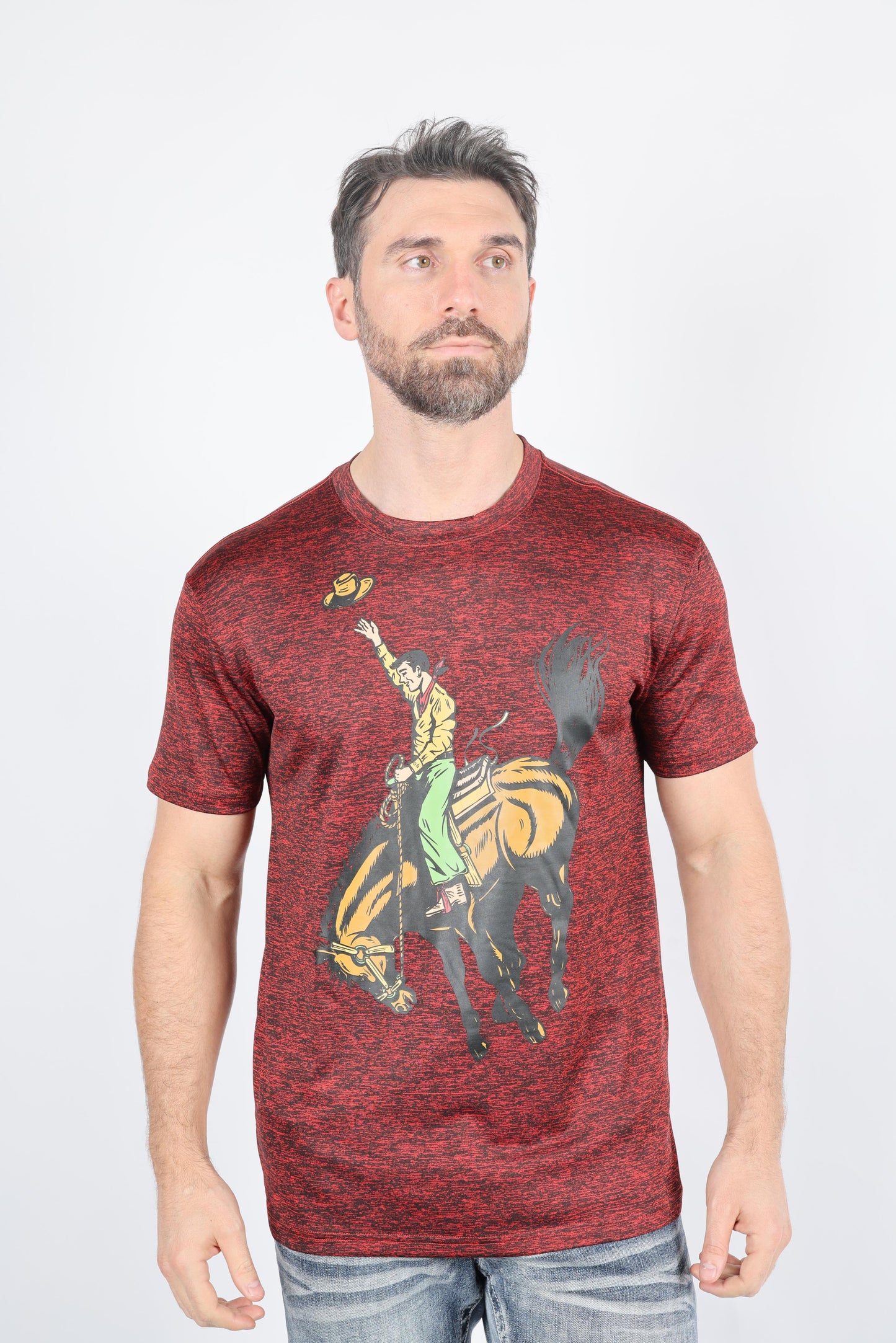 A man wearing a heathered red crewneck t-shirt with a graphic of a cowboy riding a bucking horse, paired with blue jeans, against a plain light gray background.