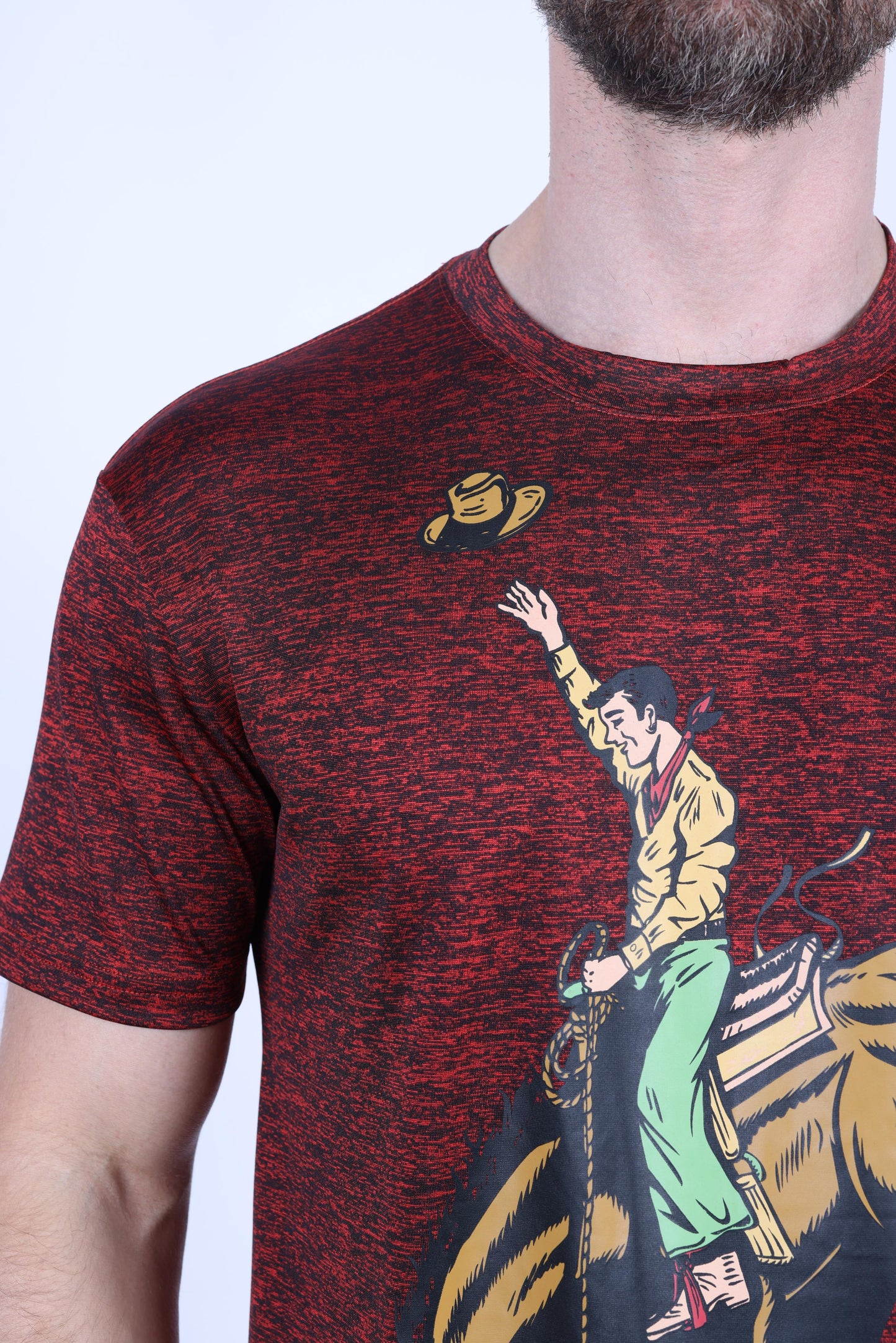 A close-up of a man wearing a short-sleeve crewneck t-shirt with a red and black heathered texture. The shirt features a graphic print of a cowboy riding a bucking bronco, with a yellow hat flying off.